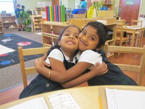 Two girls in a daycare setting hugging.